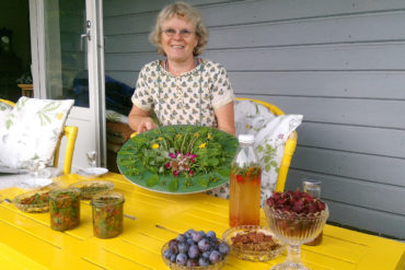 Kvinne viser frem mat av bær og planter fra egen hage.