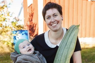 Kvinne med baby på en arm og en stor squash i den andre.