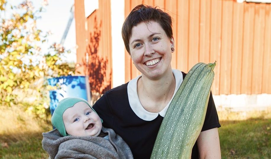 Kvinne med baby på en arm og en stor squash i den andre.