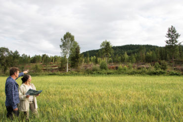 En kvinne og en mann på et åpent jorde peker opp mot et potensielt boligområde.