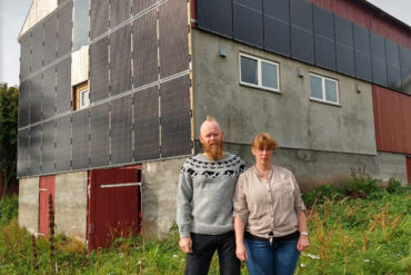 Kvinne og mann foran driftsbygning med solcellepaneler på veggene.