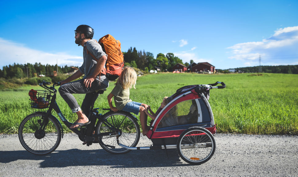 Mann på sykkel med tilhenger i landlig sommerlandskap