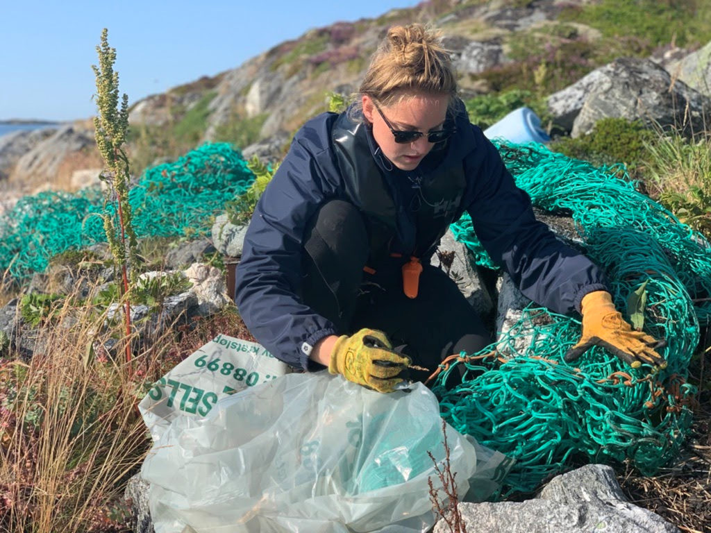 Kvinne i sjøkanten rydder plast- og fiskeutstyr