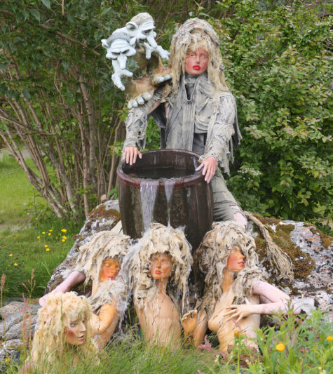 Kunstinstallasjon med dukke bak tønne og dukker av kvinner i gresset i forkant