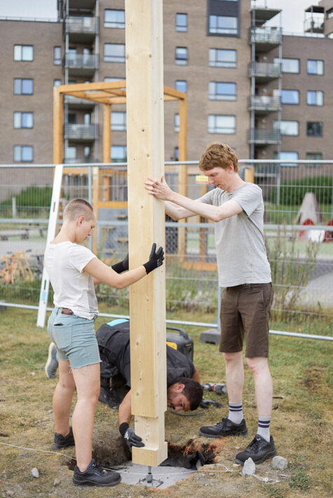 To mennesker holder treverk oppe på en plass foran en bygning.