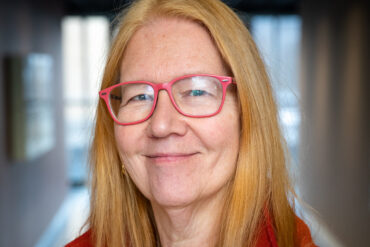 Person med langt hår og rød jakke i korridor