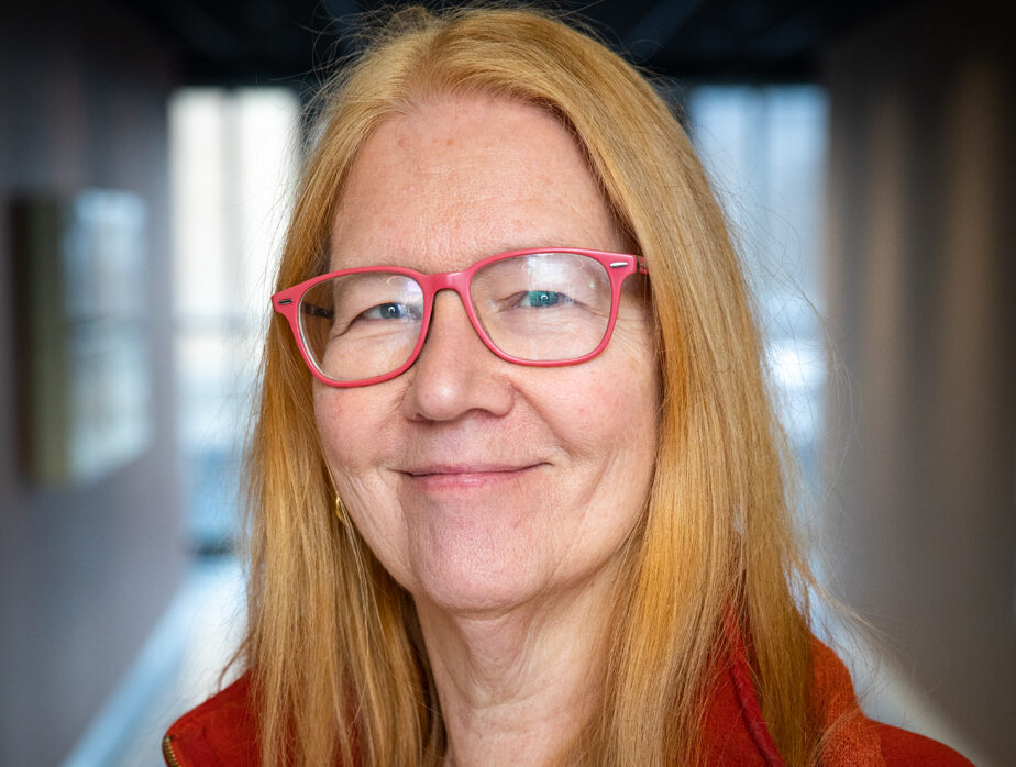 Person med langt hår og rød jakke i korridor