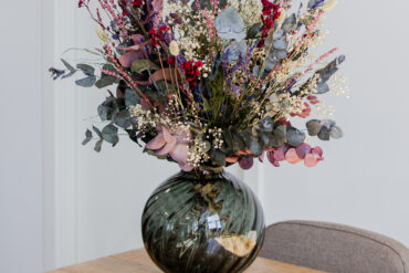 Blomsterbukett i mørk vase på lyst trebord