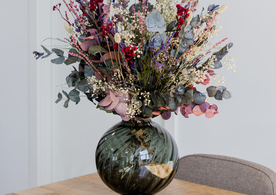 Blomsterbukett i mørk vase på lyst trebord