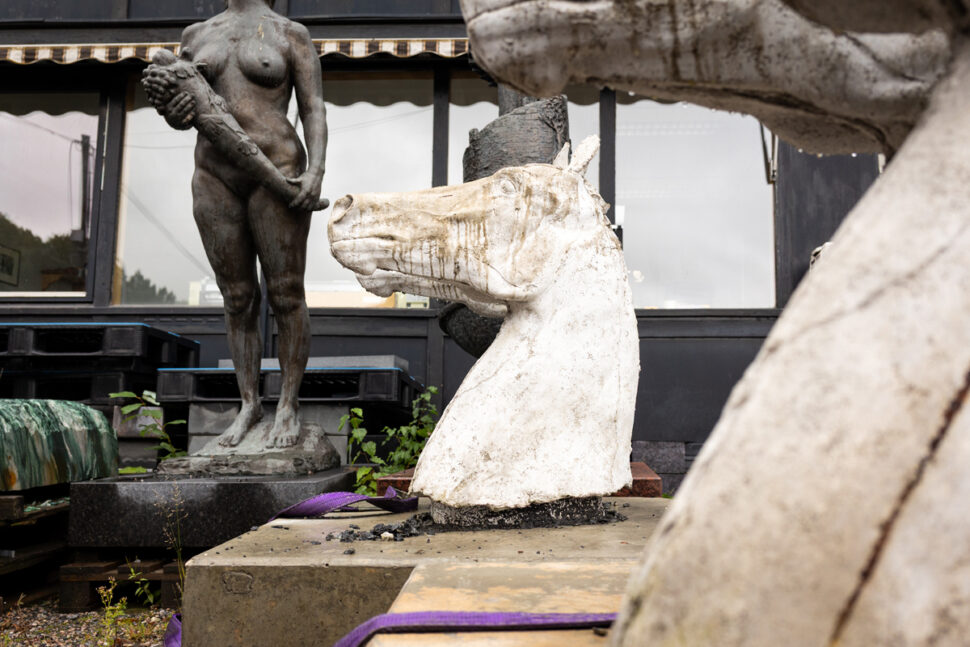 Steinskulpturer av hestehode og menneskekropper plassert foran vindusflater på hus.