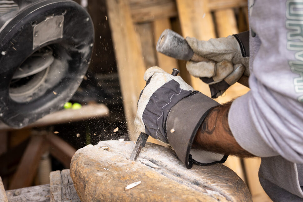 Hånd holder redskaper for å forme steinskultptur.