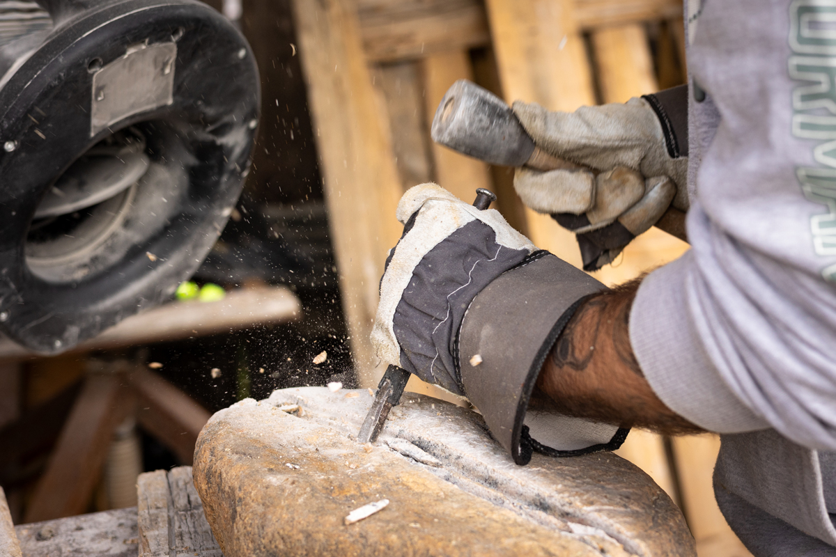 Hånd holder redskaper for å forme steinskultptur.
