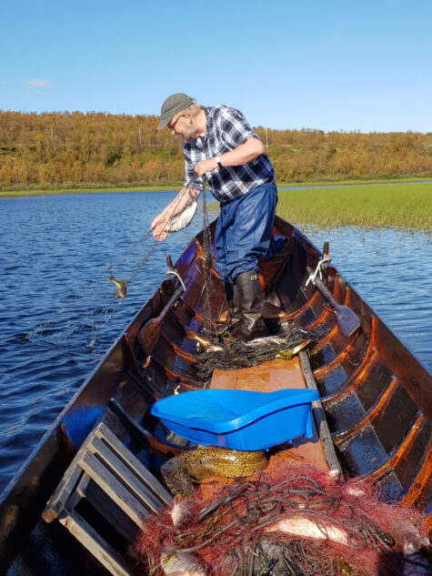 Person drar garn fra båt på elv med vidde i bakgrunnen.