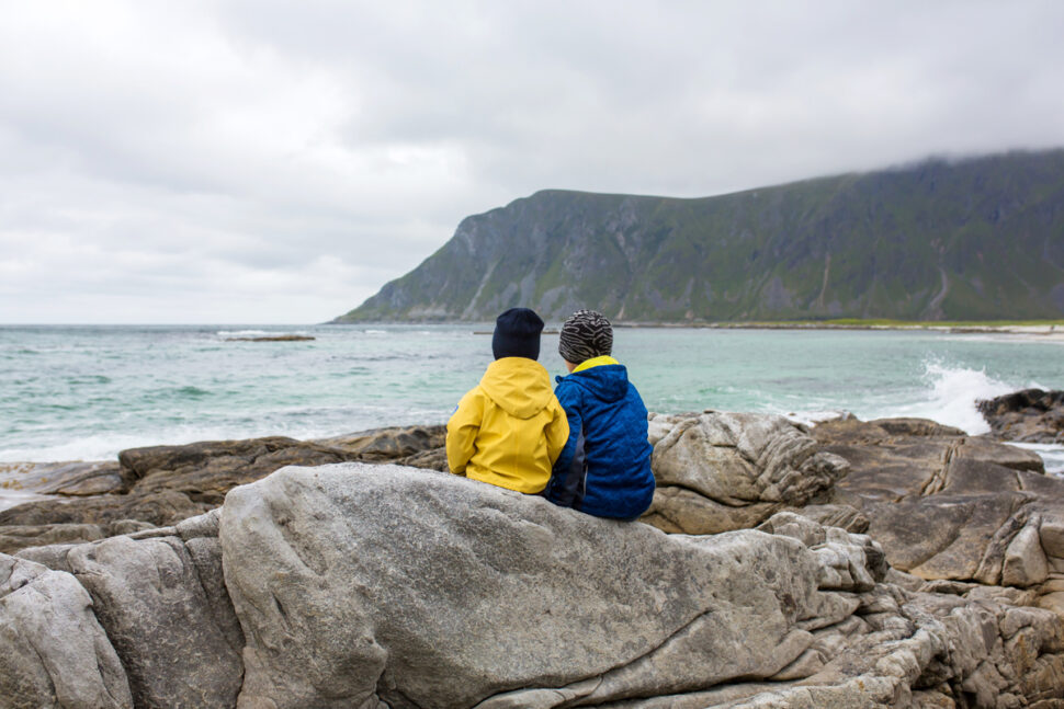 To barn sitter på svaberg og ser ut over fjord med fjell i bakgrunnen.